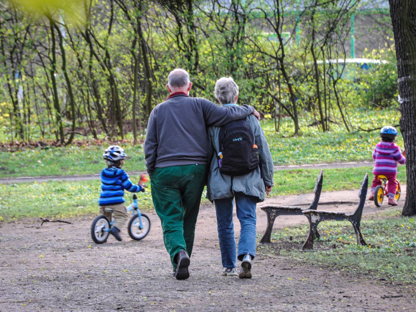Ein Großeltern-Paar geht spazieren, vor ihnen fahren zwei Kleinkinder auf einem Laufrad.